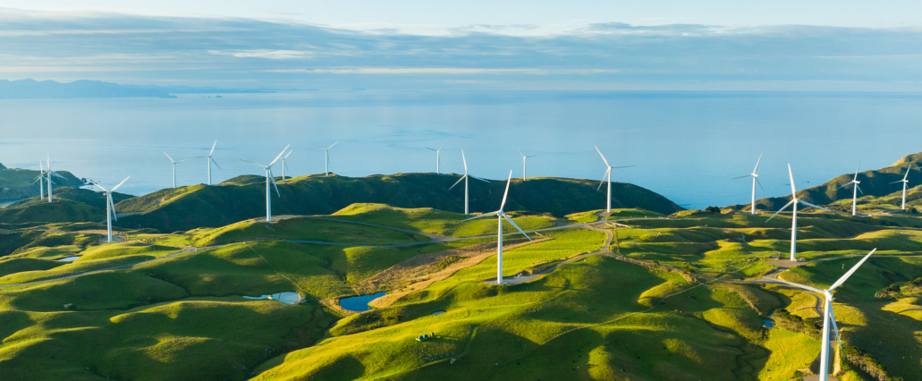 Wind turbines on rolling green hills with a view of the ocean at sunset, symbolizing renewable energy and sustainability in California's dynamic pricing pilot programs.